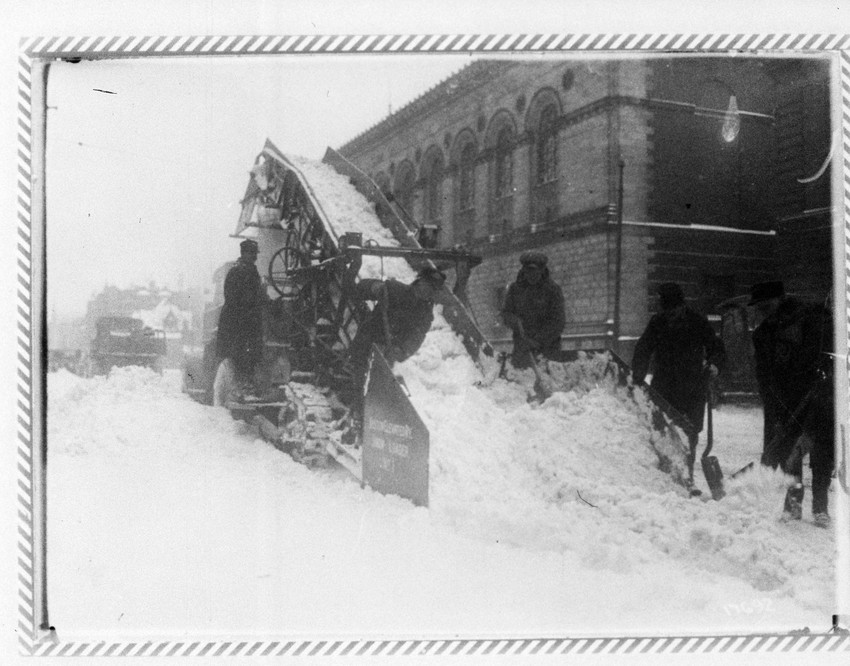 Men shoveling snow onto snow conveyor