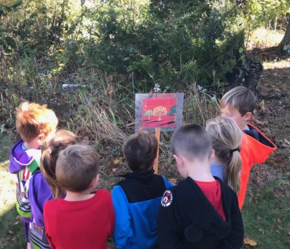 A group of seven students gather around a storybook page outdoors.