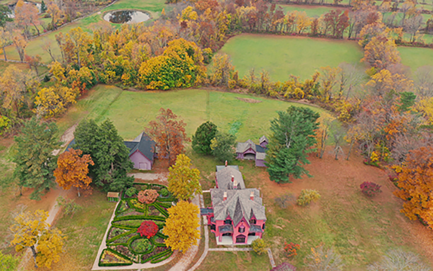 Overhead view of the pink Roseland Cottage showing autumn landscape, outbuildings, and garden