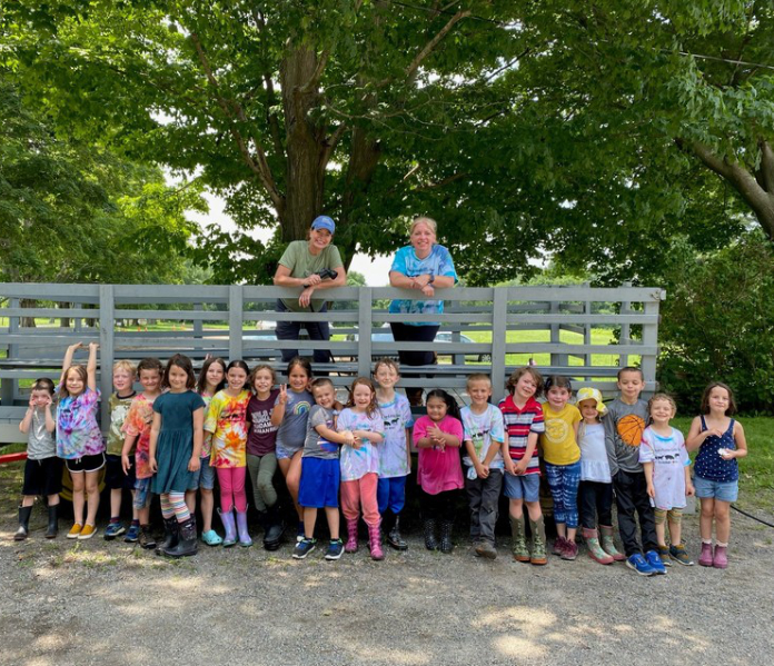 Group of children stand in front of a wagon on a farm.