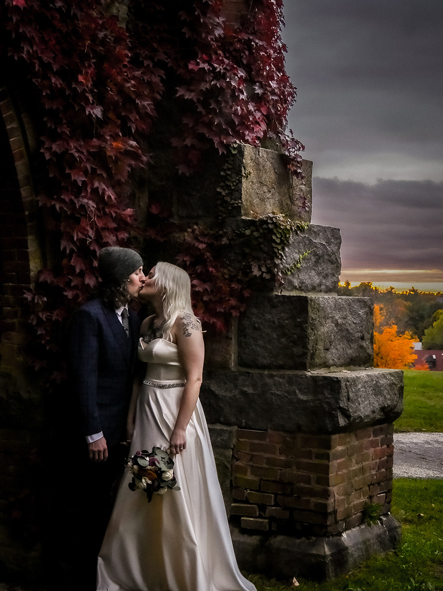 Bride and groom on an autumn evening near an ornate brick pillar.