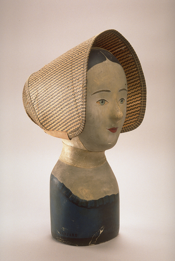 Carved wooden woman's head for a milliner. Neck painted white, painted  black hair with paper eyebrows, eyes, and lips.