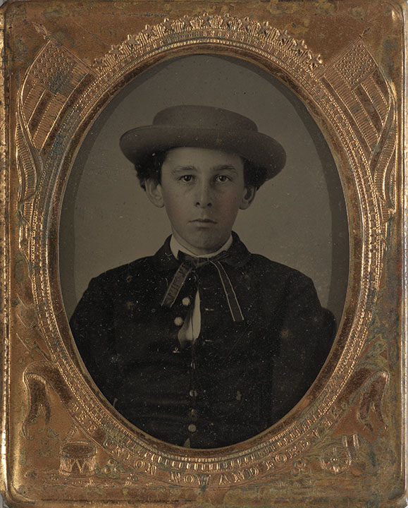 Oval framed black and white picture with some hand coloring of boy wearing formal attire.