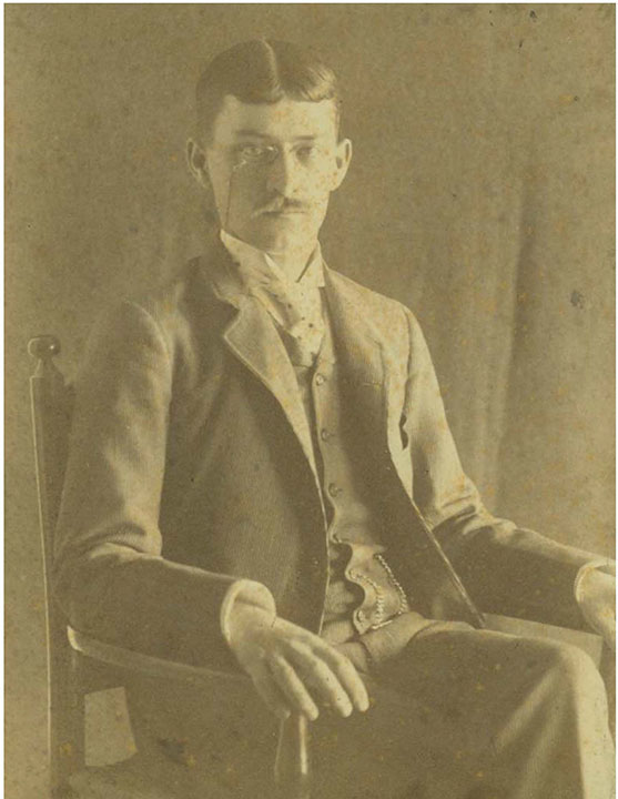 Black and white picture of seated man with mustach and glasses