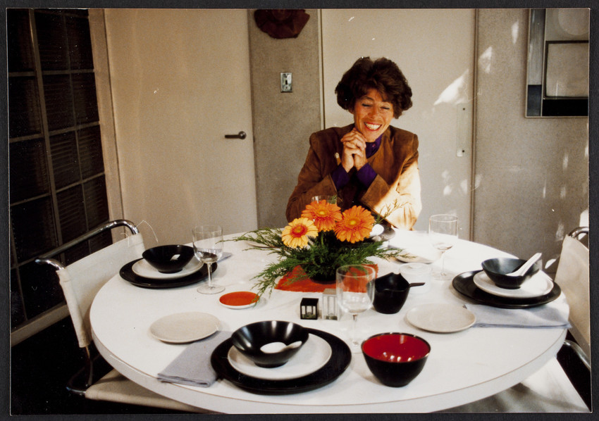 Ati Gropius sitting at the dining table at the Gropius House, set with dishes and a bouquet of Gerber daisies