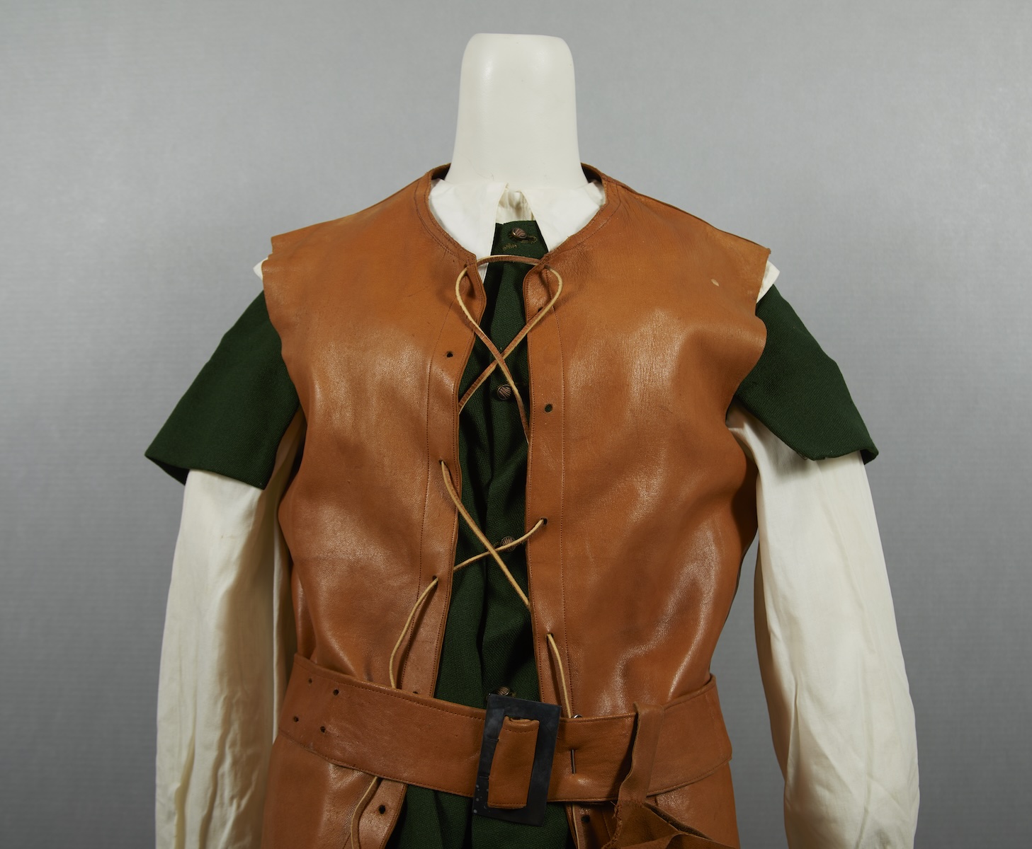 A costume featuring a brown leather vest over a green and white tunic, displayed on a mannequin against a neutral background.
