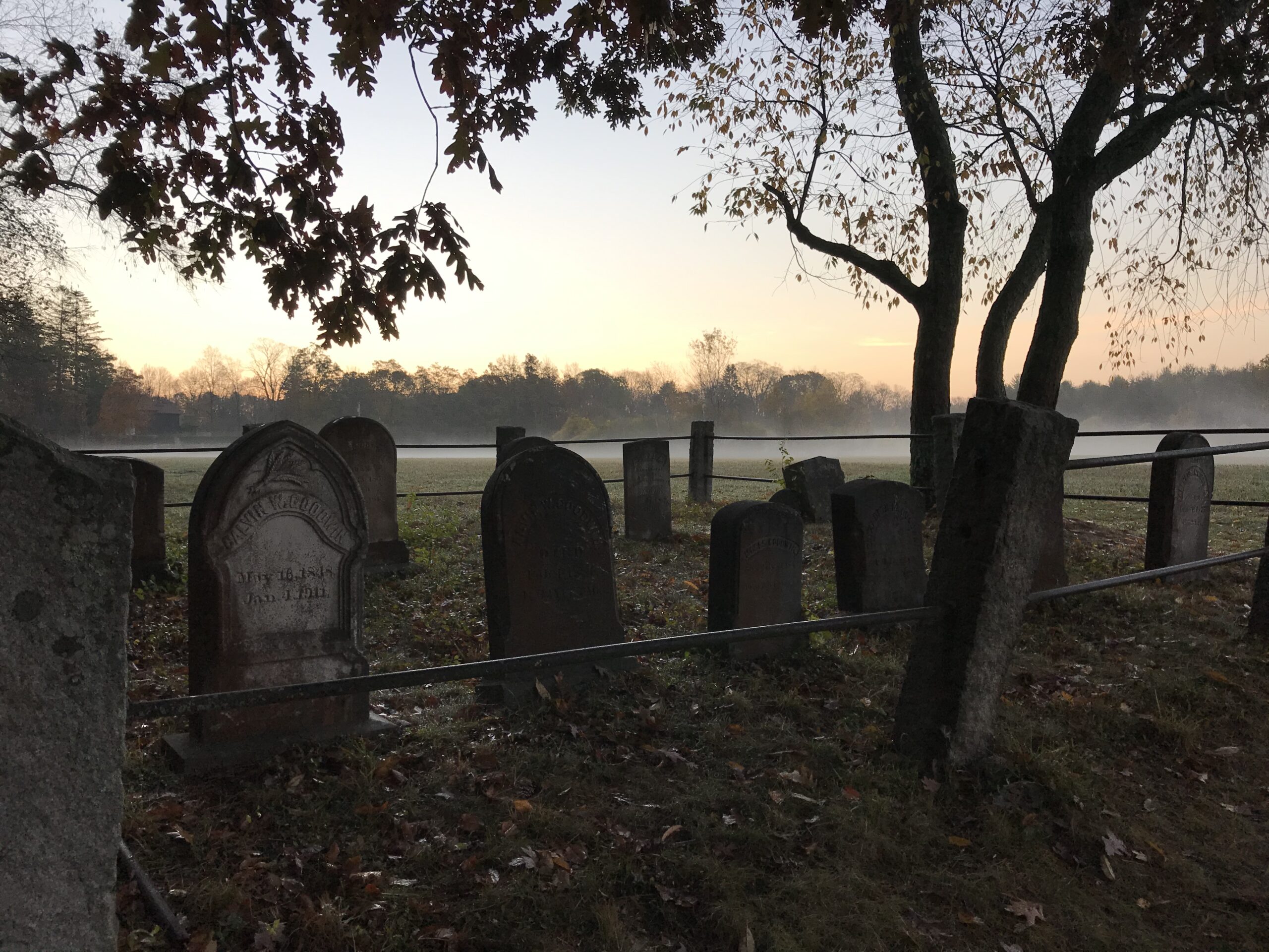 Small cemetery with several headstones at dusk. Cemetery is fenced.