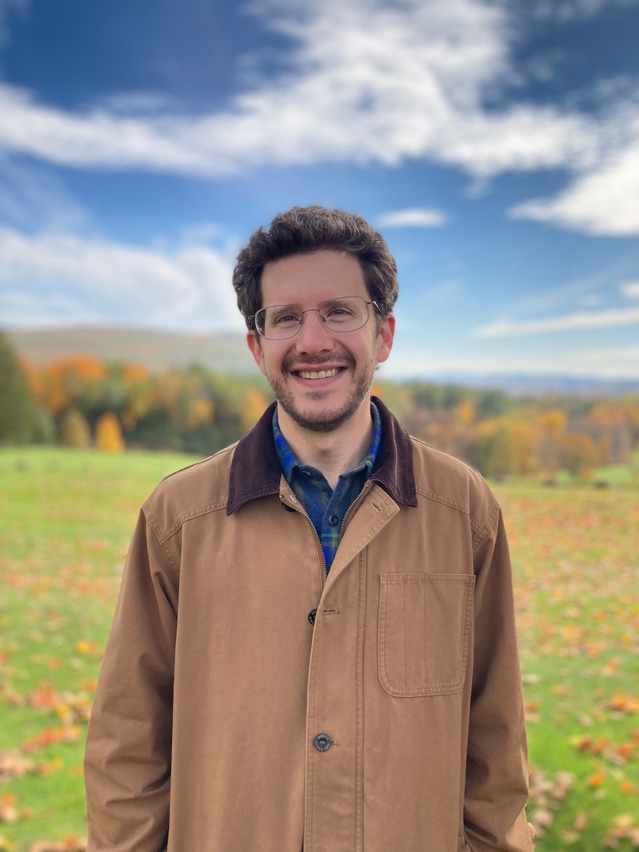 Person in tan jacket standing in front of grassy mountain range