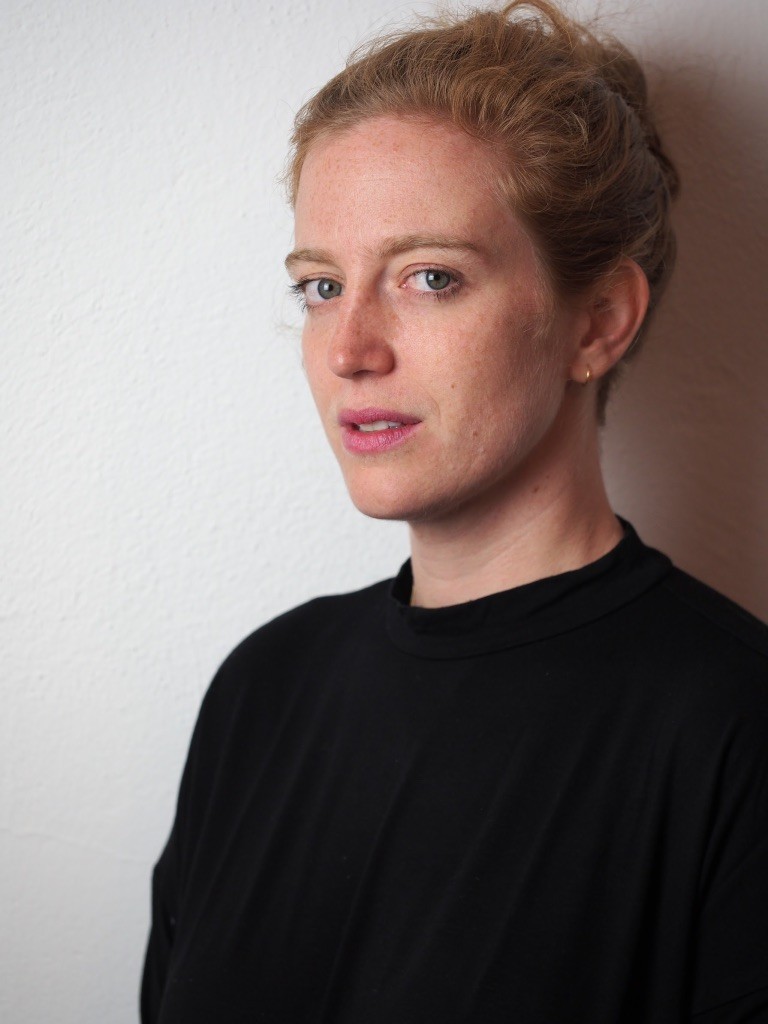 Person in black top leaning against white wall