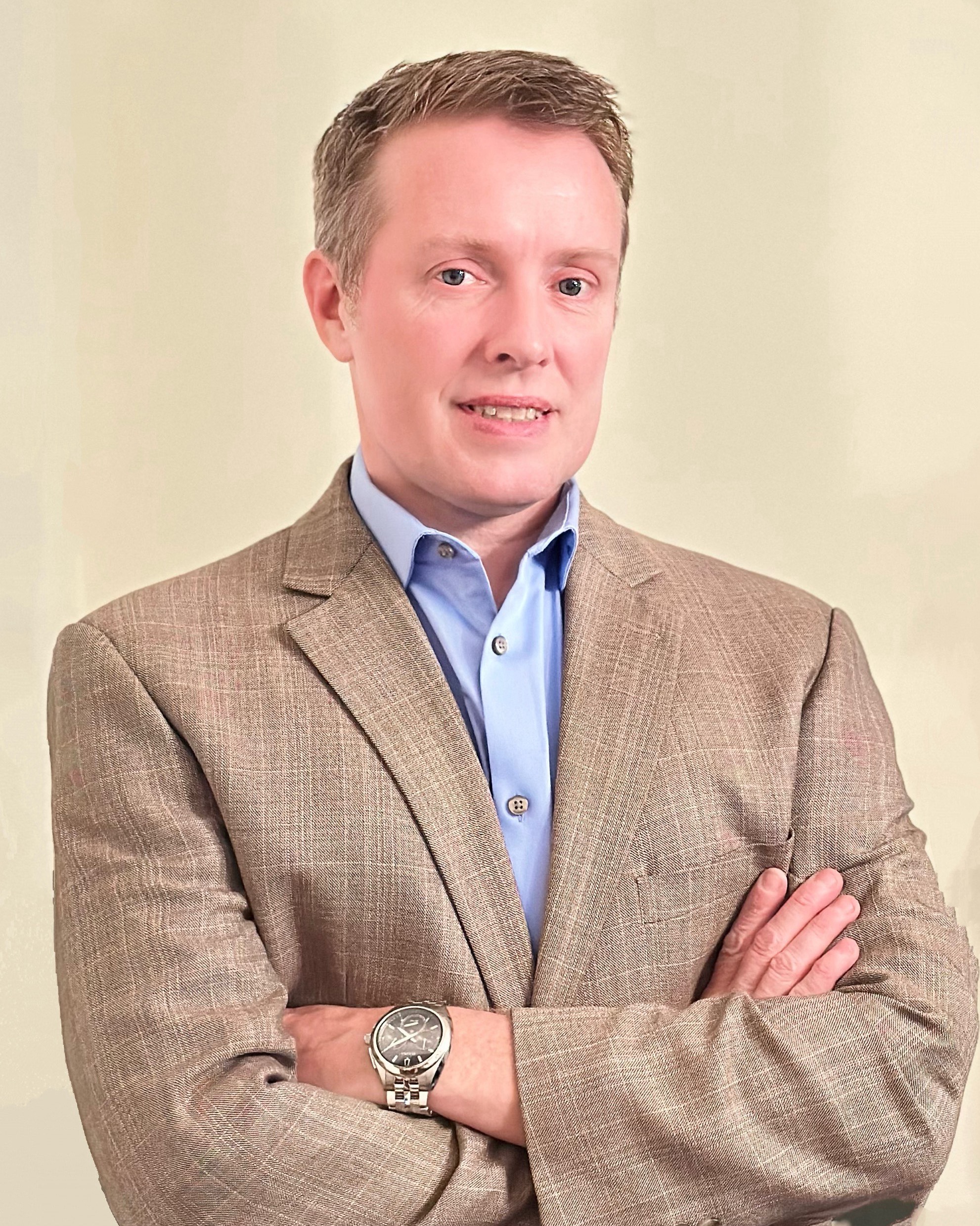 Person standing in front of beige background in sportcoat with arms crossed
