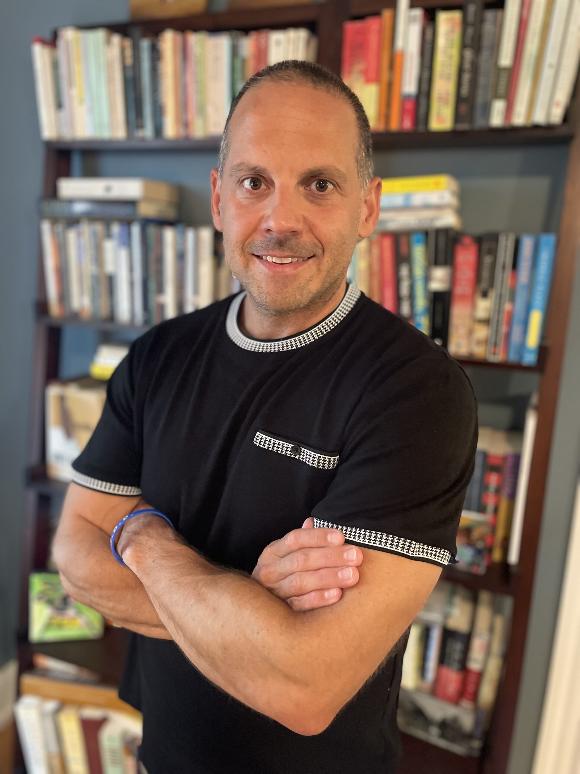 Person standing in front of bookcase with arms crossed