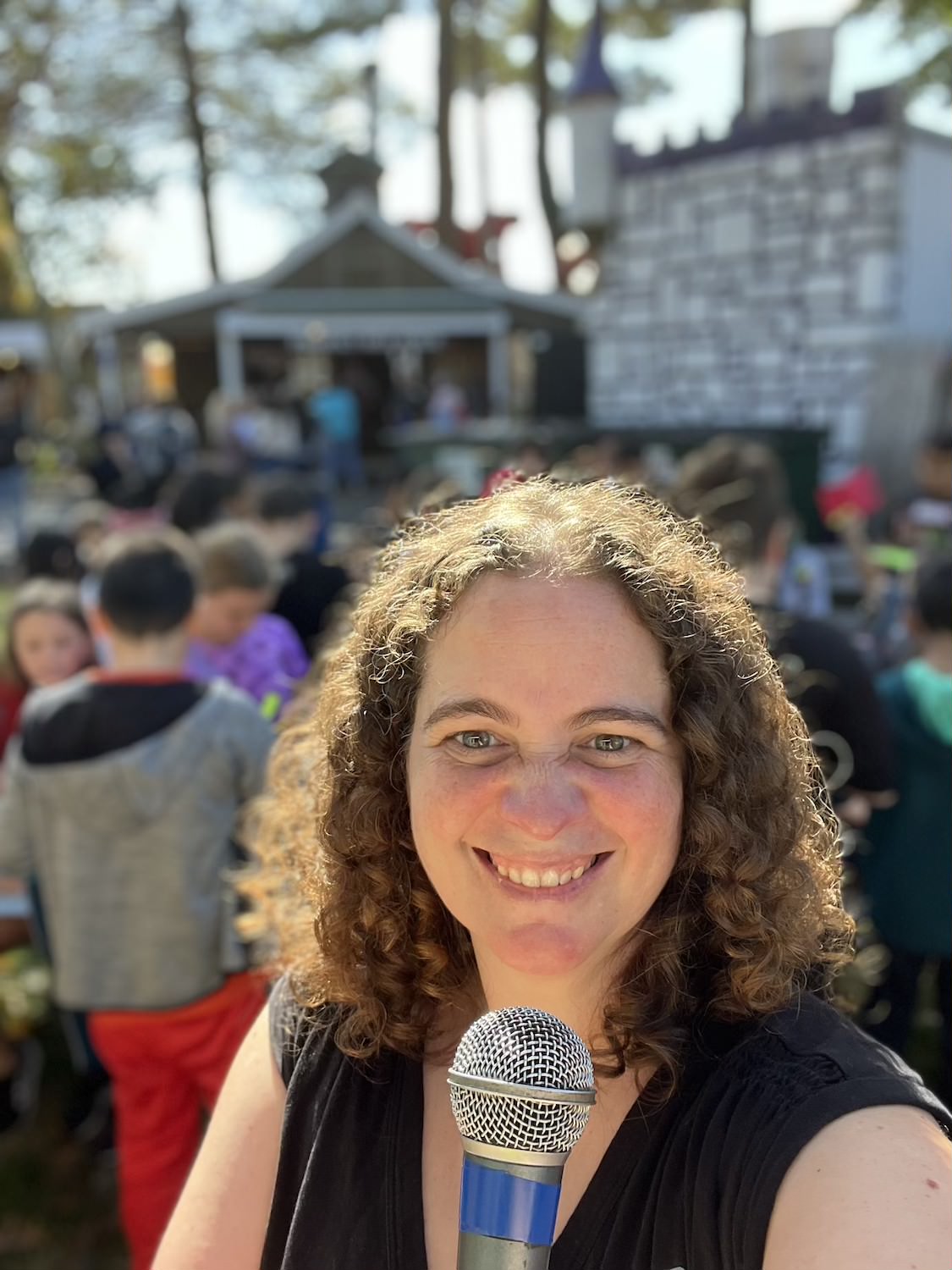 A smiling woman with curly hair holds a microphone.
