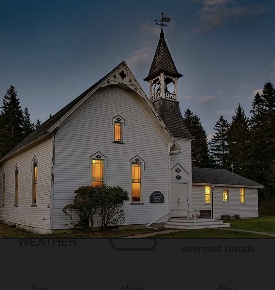 White clapboard building with bell tower. Lit from within.