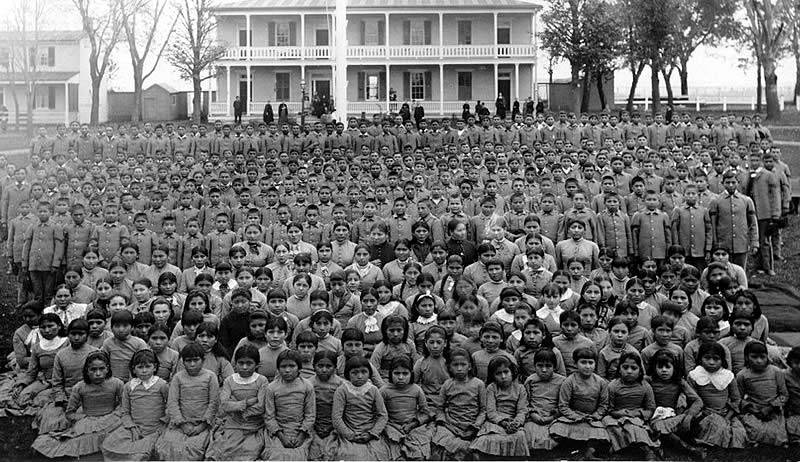 Rows of school children in front of white two story building.