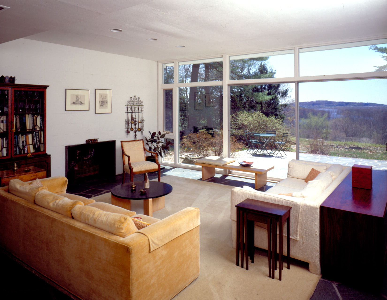 Midcentury modern living room with large windows and vintage furniture, overlooking a scenic view.