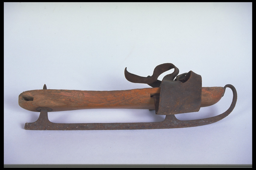 A wooden ice skate with metal blade and leather strap at front.
