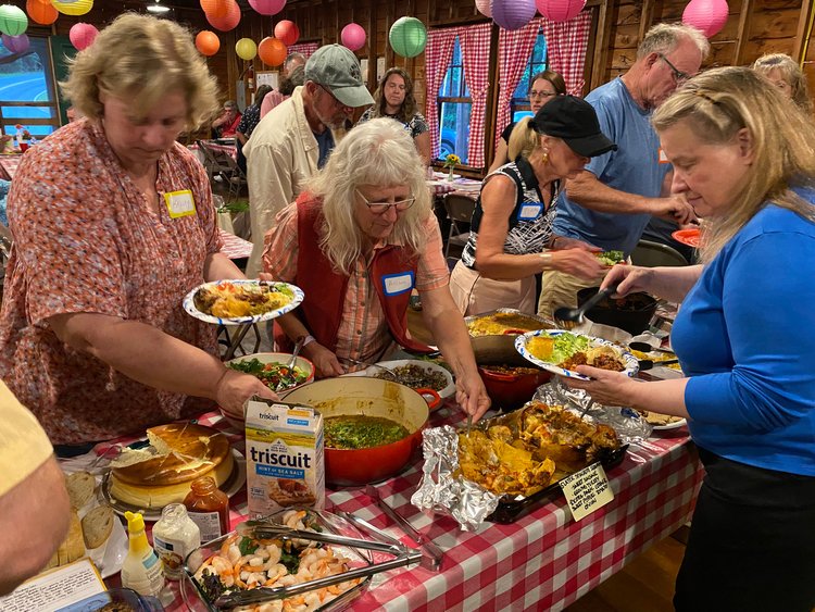 People serving themselves at a buffet with various dishes in a rustic indoor setting.