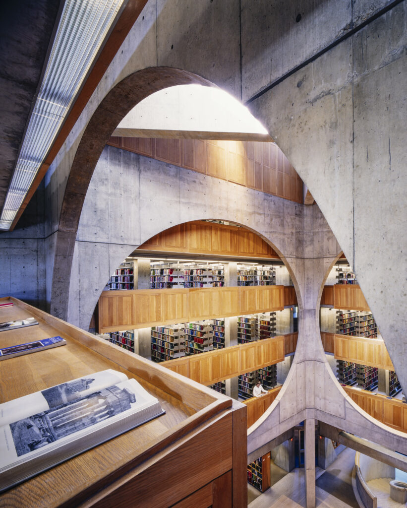 Interior of a modern library with large concrete arches and wooden bookshelves.