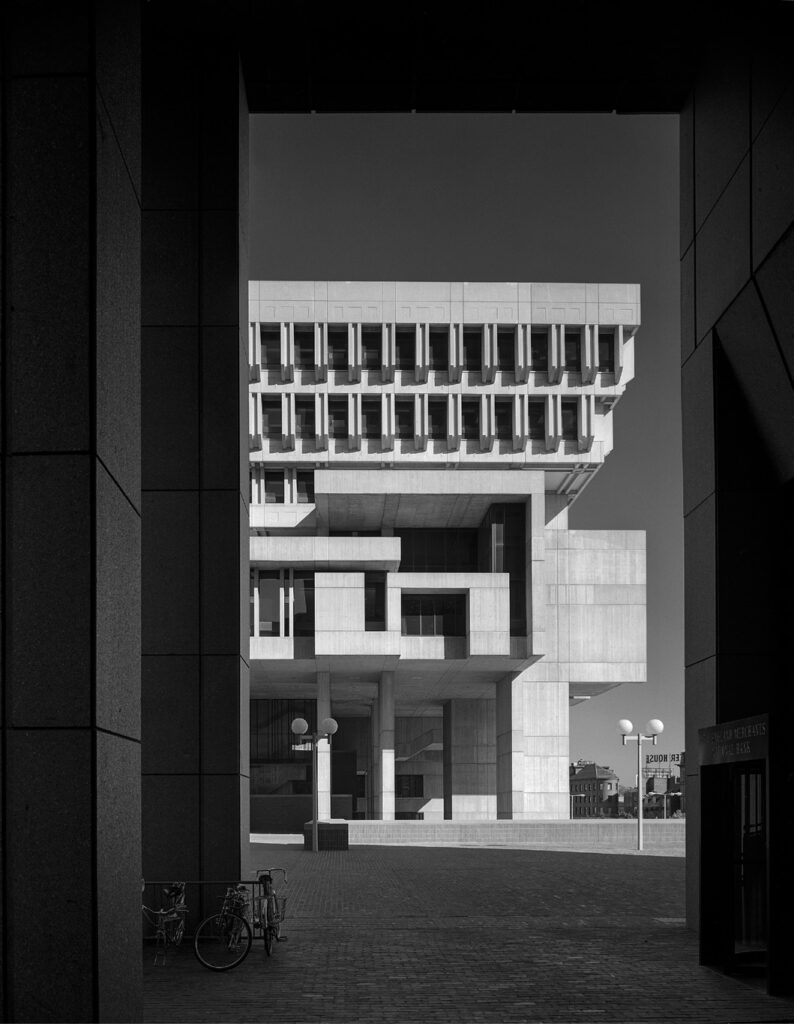 View of a Brutalist concrete building framed by darker structures with bicycles and spherical lamps in foreground.