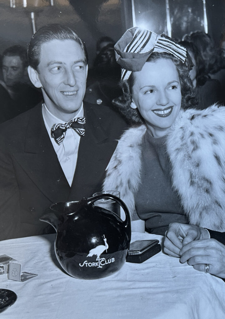 A man and woman smiling at a table with a "Stork Club" pitcher. Transcribed Text: Stork Club