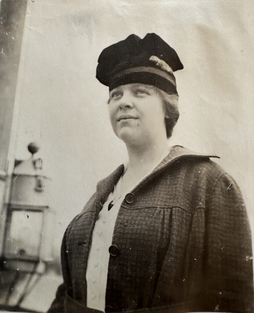 A woman in a dark coat and hat stands outdoors in a black and white photograph.