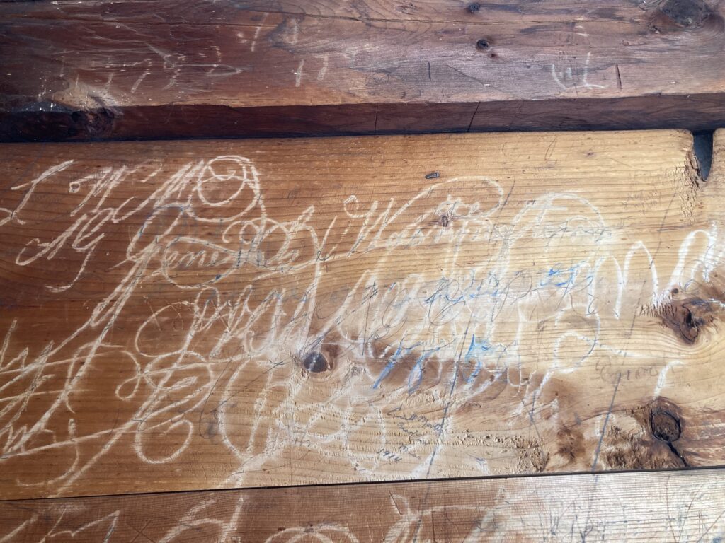 Wood wall with carved engravings and etchings in cursive and swirling patterns.