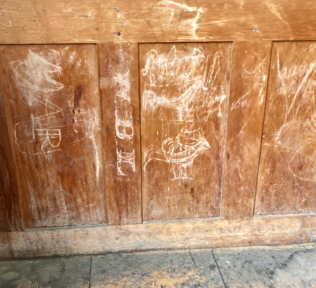 Wooden panel wall with faded chalk markings and letters.