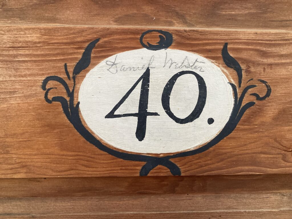 Oval sign with "40." on wooden surface with decorative flourishes. Transcribed Text: Daniel Webster 40.