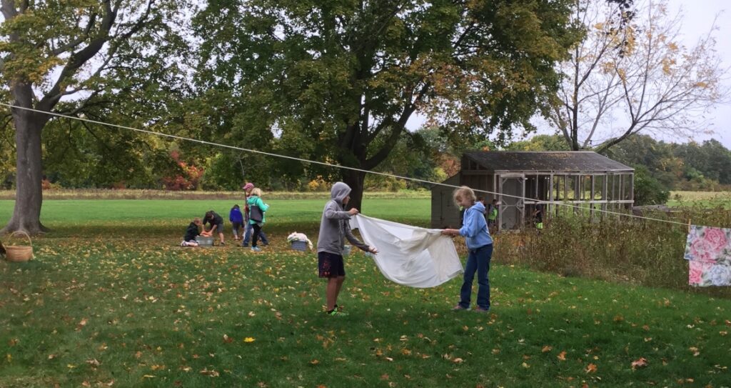Children playing with a sheet and doing activities outdoors in a grassy area with trees and a shed in the background.