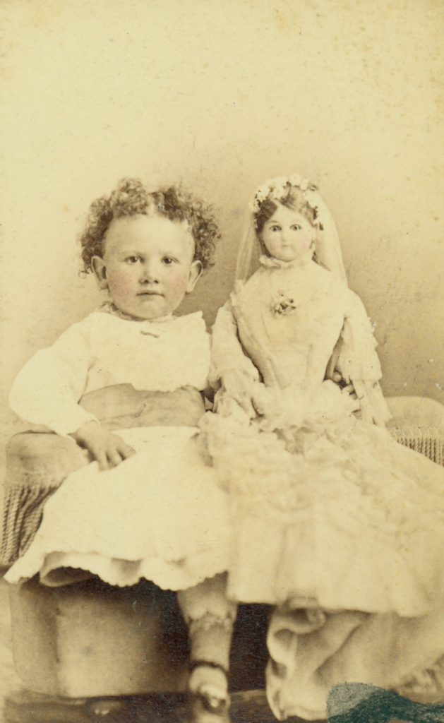 Sepia-toned photo of a young child with a doll in a bridal outfit.
