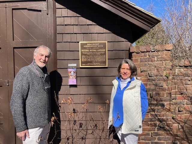 Two people standing in front of a building with a plaque and a brick wall nearby. Transcribed Text: "BEAUPORT SLEEPER-McCANN HOUSE has been designated a NATIONAL HISTORIC LANDMARK This site possesses national significance in commemorating the history of the United States of America 2003 National Park Service United States Department of the Interior"