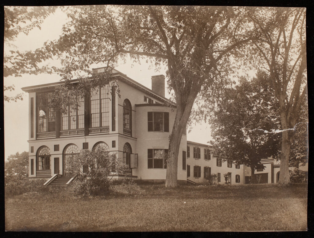 Sepia-toned photo of a large historic building with arched windows, surrounded by trees.
