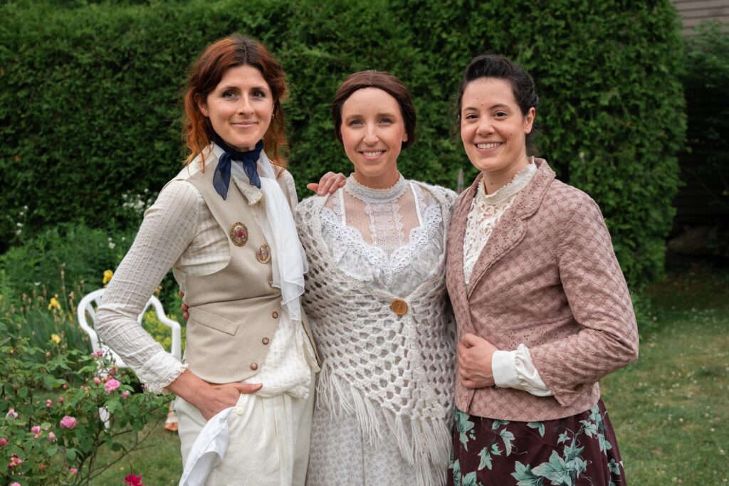 Three women in vintage-style clothing standing outdoors in a garden.