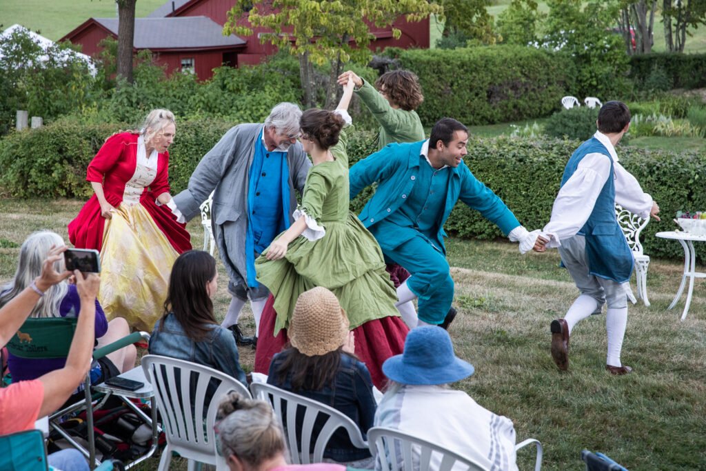 People in period costumes dancing outdoors with an audience watching.