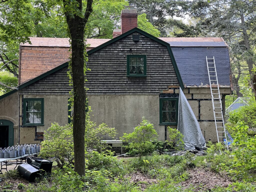 House being renovated with exposed wooden roofing, surrounded by trees and plants.