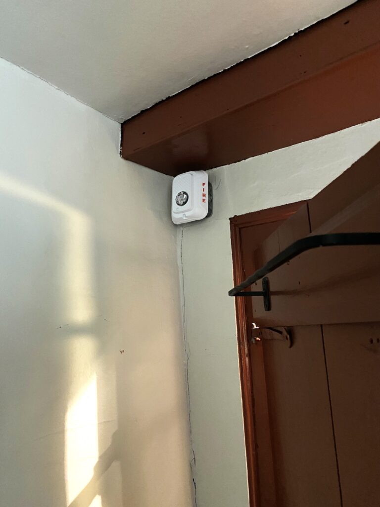 A fire alarm mounted in the corner of a room near the ceiling.
