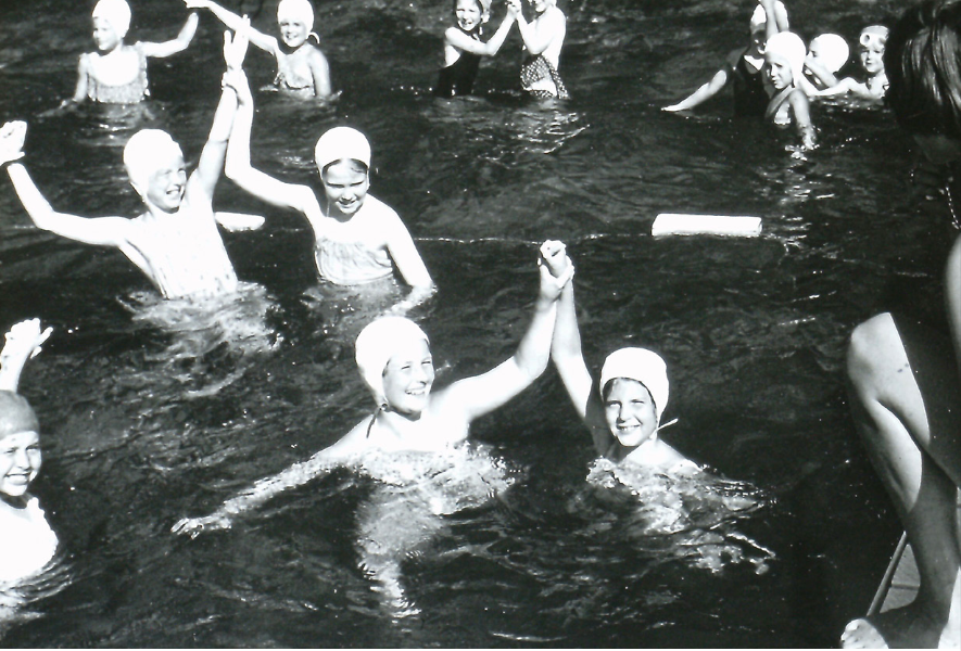 A group of people in swim caps smiling and holding hands in a pool.