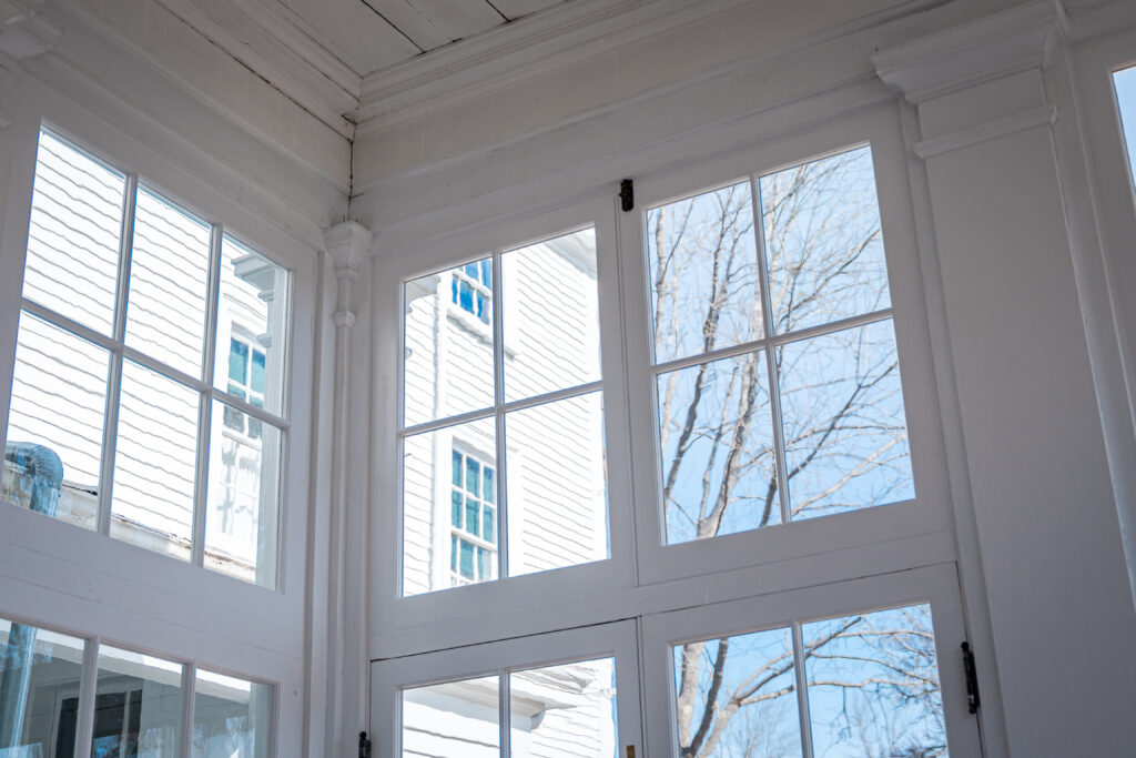 Interior view featuring large, white-framed windows with a view of a white building and tree branches outside.