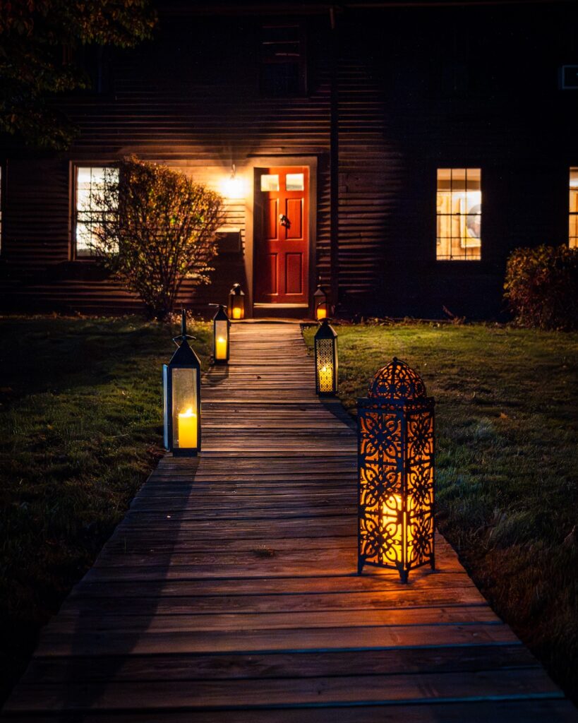 Wood walkway with decorative lanterns leading to a house with a red door at night.