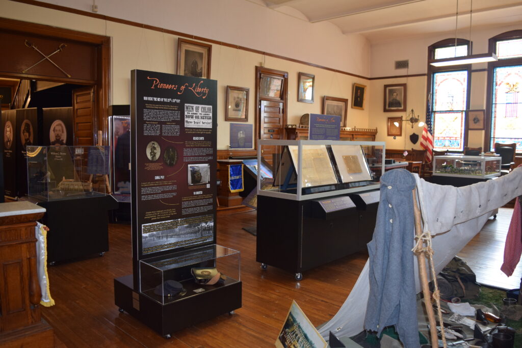 Museum exhibit room with historical displays and artifacts. Transcribed Text: “Pioneers of Liberty.” "Men of Color Now On Reward." Other text includes descriptions of historical events and figures.
