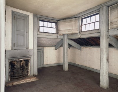 Old attic room with windows, wooden beams, and a fireplace.