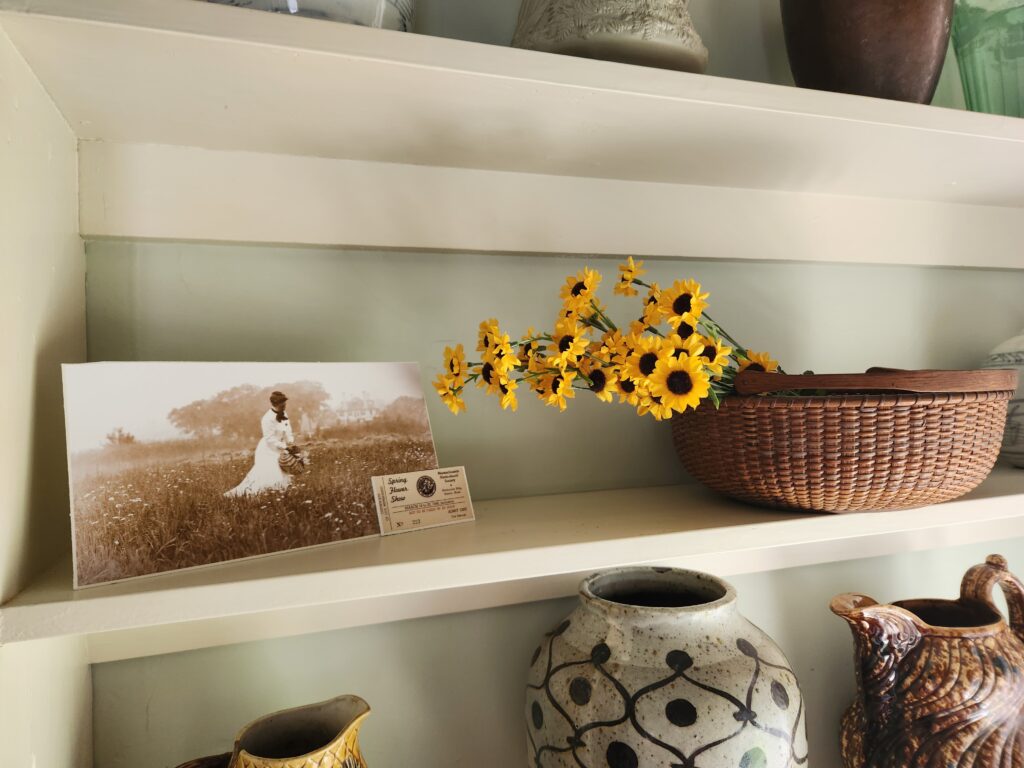Shelf with a historical photo, wicker basket of yellow flowers, and decorative ceramics.