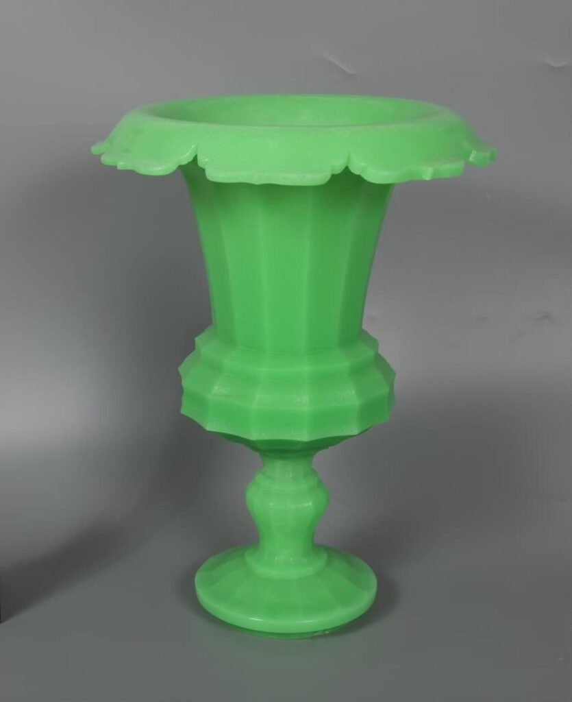Green fluted urn with scalloped rim and pedestal base against a gray background.