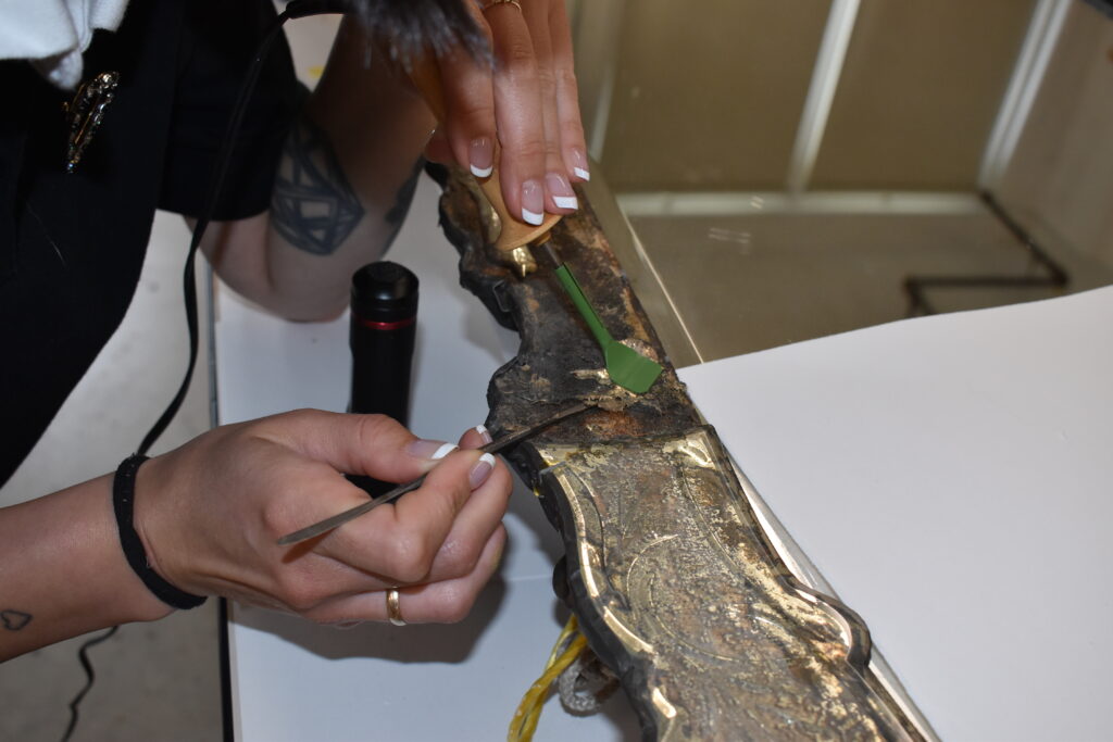 Person restoring a corroded decorative object using small tools.