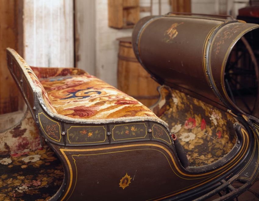 Vintage sleigh with ornate floral designs and colorful tapestry upholstery indoors.