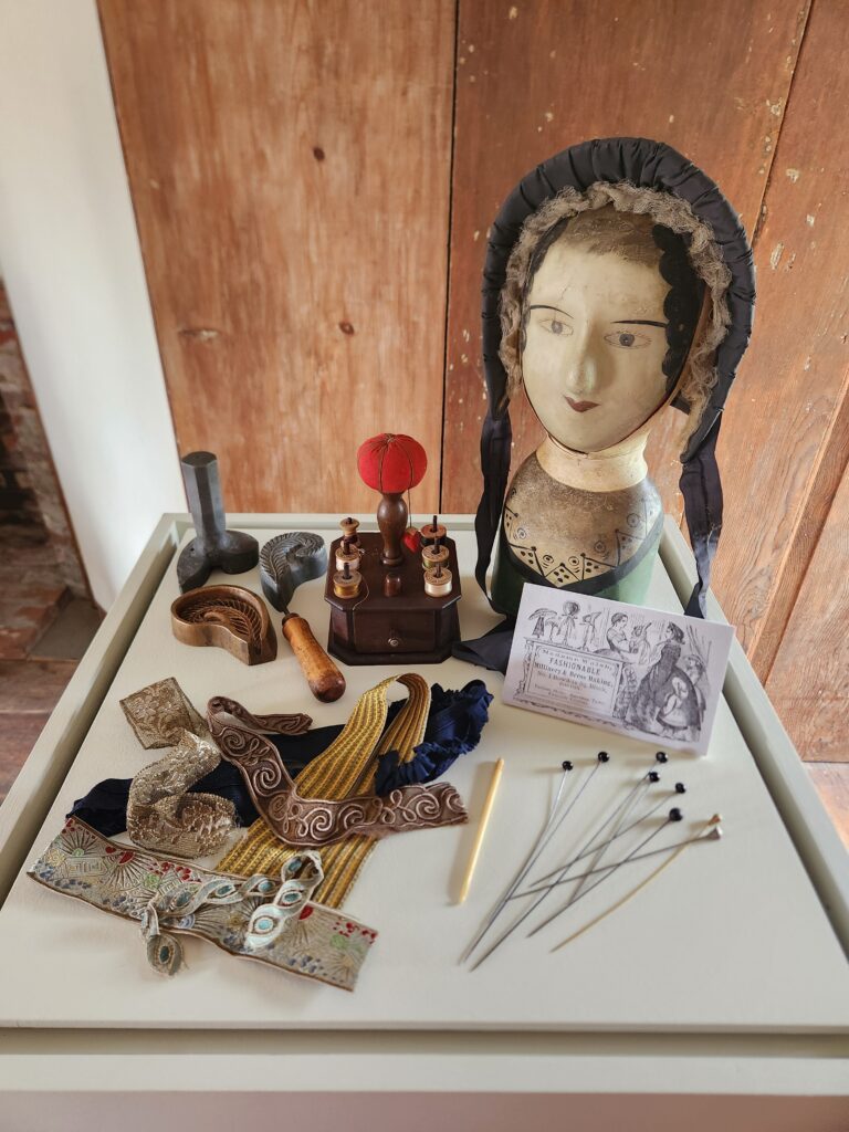 Collection of historical millinery tools and fabrics displayed with a mannequin head wearing a bonnet.