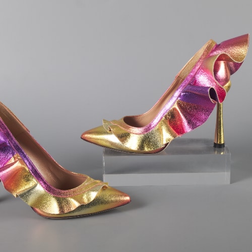 A photo showing gold and reddish pumps with ruffles. One is placed upon a small pedestal.