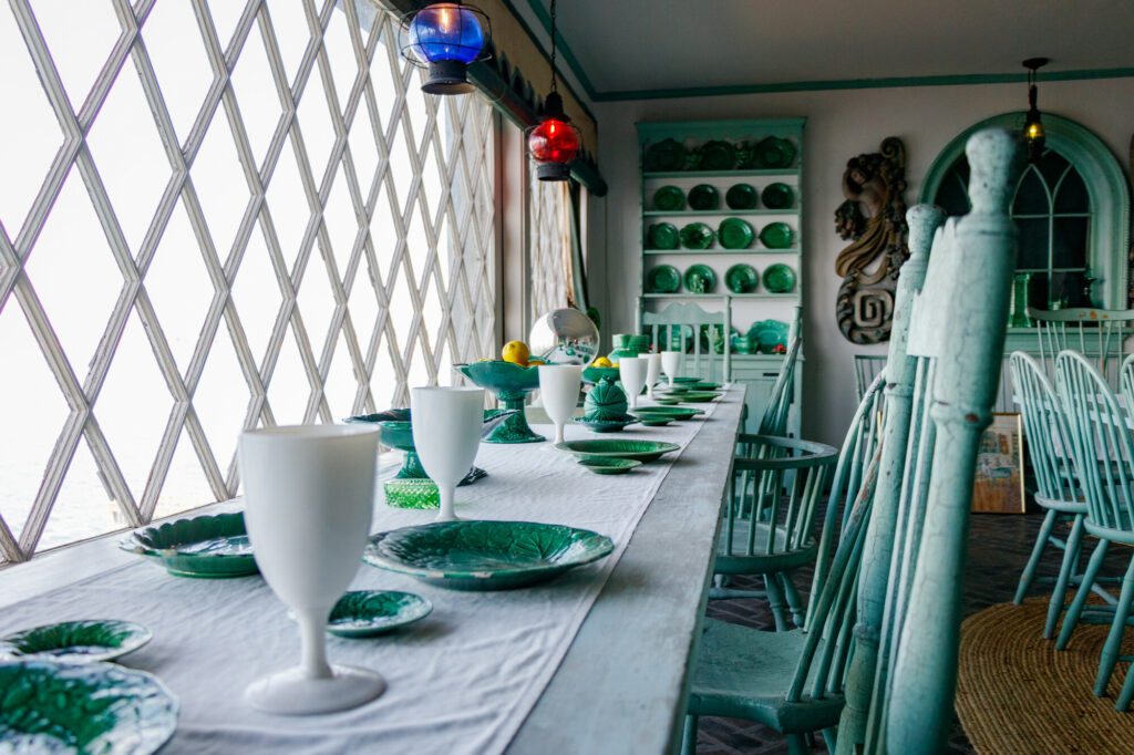 Elegant dining room with a long table, green dishware, and vintage chairs. Large diamond windows create an airy space.