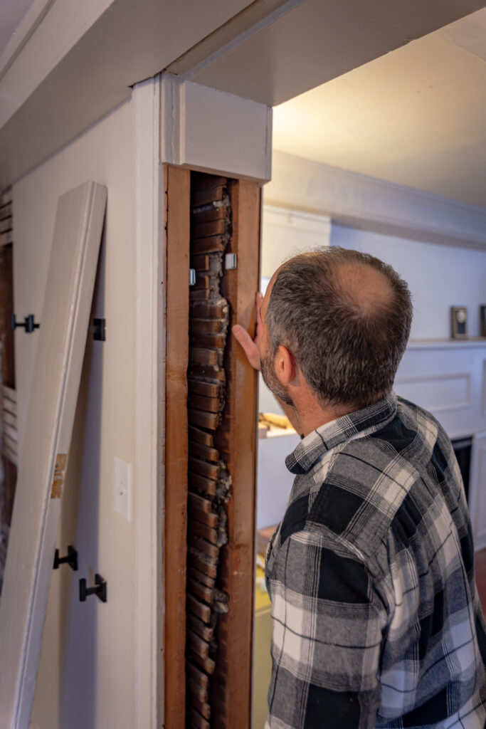 Man examines exposed lath and plaster wall in a historic building, showcasing traditional architectural techniques.