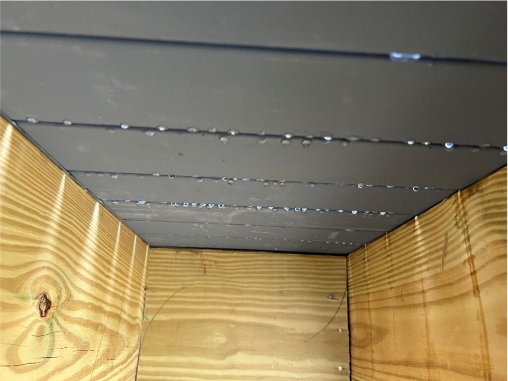 Water droplets on a sleek, modern metal ceiling above light wood paneling. Simple and elegant architectural design.